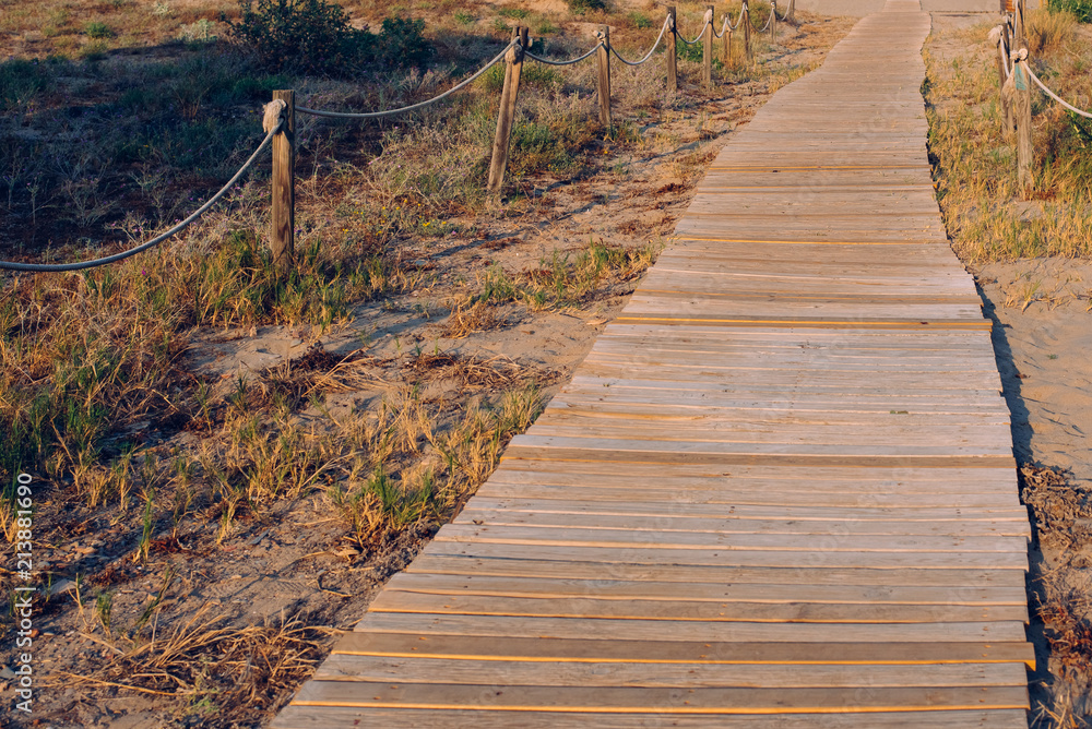 Fototapeta premium wooden path through the dunes towards a summer beach at sunset