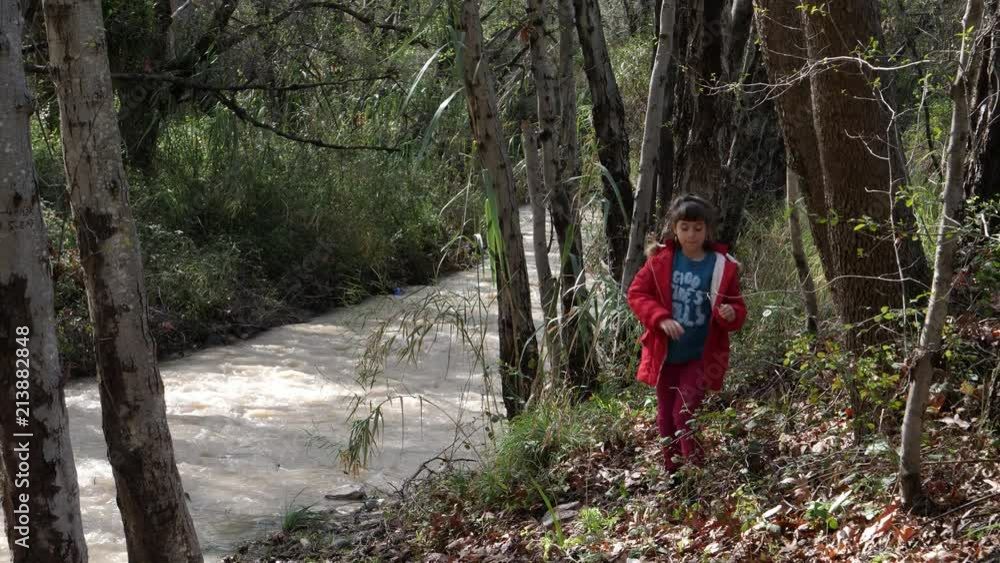 Little girl has a hard time walking on an uneven riverbank in a forest Little girl has a hard time walking on an uneven riverbank in a forest