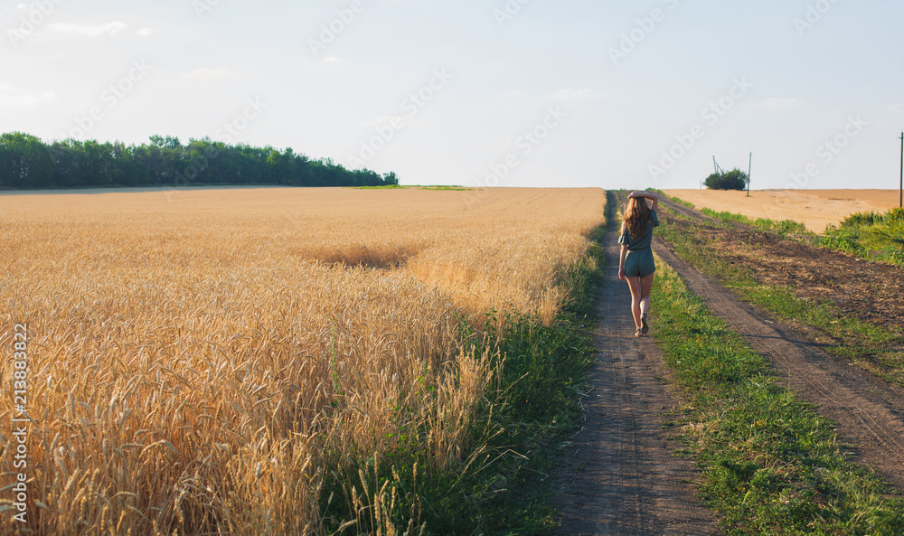 Happy Young Woman Walking in a Wheat Field at Sunset. Agricultural Landscape. Harvest Season Concept