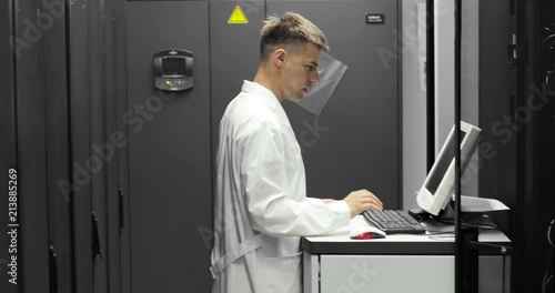 IT Technician Works on a compuiter in Big Data Center full of Rack Servers. He Runs Diagnostics and Maintenance Stets up System. photo