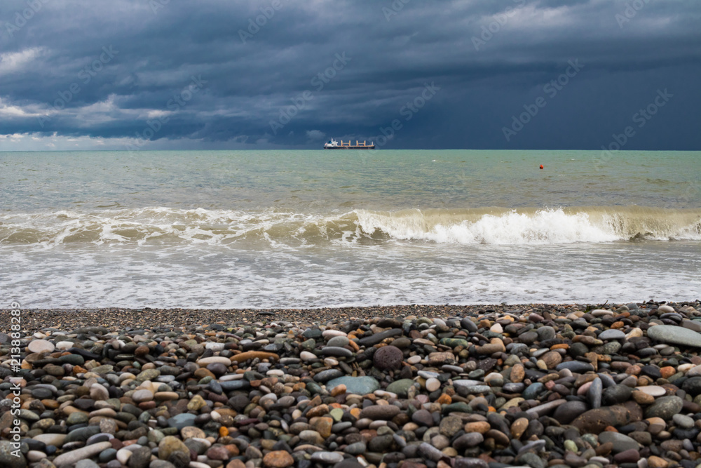 Beautiful beach view with dramatic sky of subtropical coastline in Batumi, Georgia Black Sea resort city with cargo ship moving on the horizon.