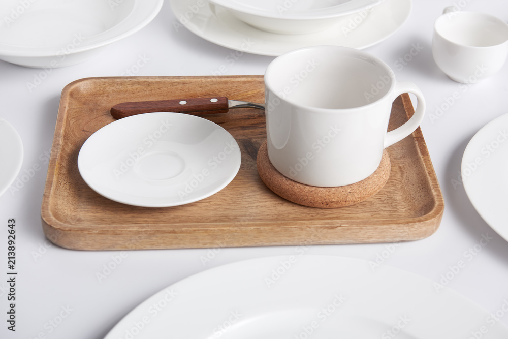 close up view of wooden tray, various plates and bowl with cup on white table close up view of wooden tray, various plates and bowl with cup on white table
