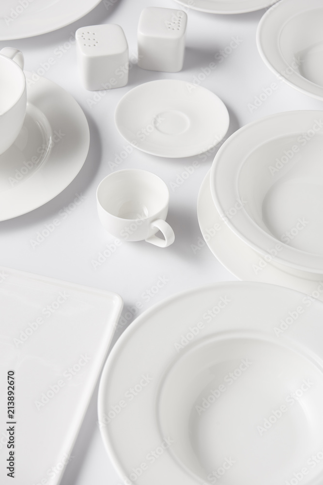 high angle view of different plates, cups, saltcellar and pepper caster on white table high angle view of different plates, cups, saltcellar and pepper caster on white table