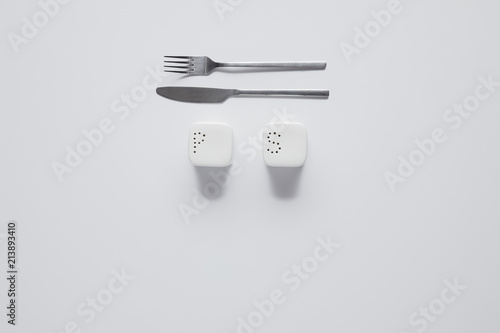 top view of fork  knife  saltcellar and pepper caster on white table  minimalistic concept