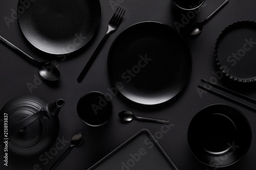 top view of black teapot, plates, bowl, cups, tray, spoons, chopsticks, fork and baking dish on black table