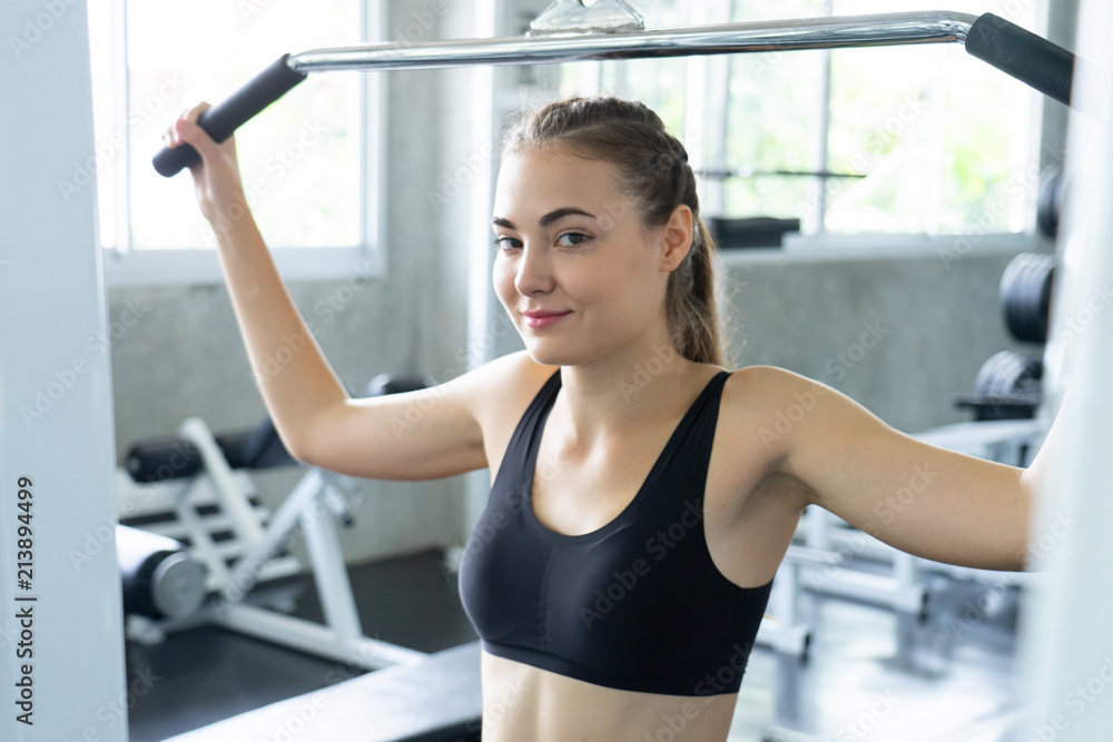 Fototapeta premium Muscular young woman with beautiful body doing exercises with dumbbell. Sporty girl lifting weights in gym.