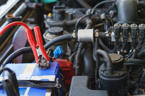 Technician check car system. Mechanic using battery jumper cables to charging battery in car garage.