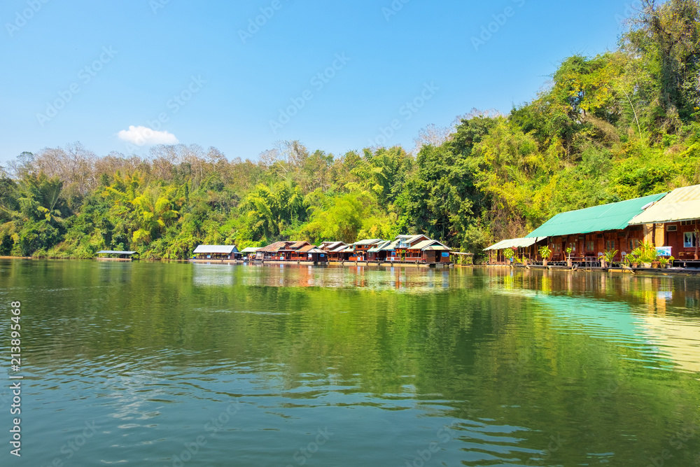 View of Wooden house raft floating in Saiyok river kwai at Kanchanaburi Thailand with blue sky and green forest. Beautiful landmark in Asia.