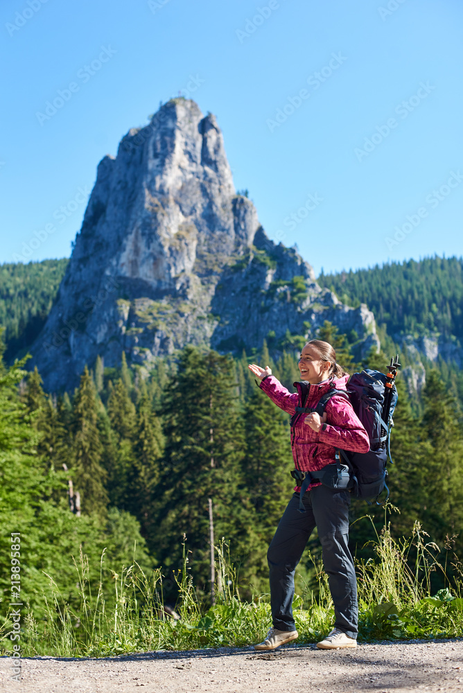 Happy tourist female with a backpack in Cheile Bicazului-Hasmas National Park Romania. A beautiful landscape of mountains, forests and blue sky above them on a sunny day