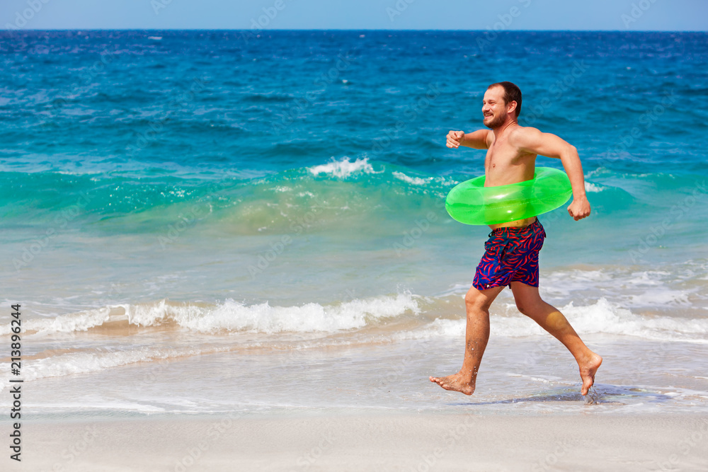 Happy bearded hipster in inflatable ring have fun on beach walk. Funny man run along sea Happy bearded hipster in inflatable ring have fun on beach walk. Funny man run along sea