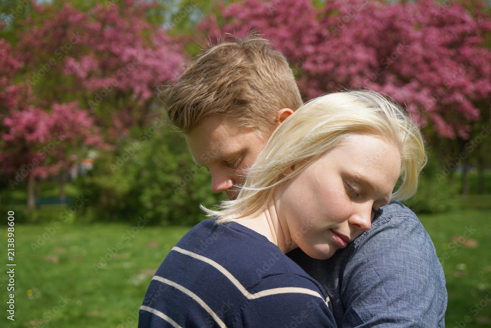 young couple embracing with her head on his shoulder in a park