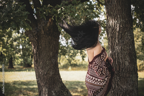 Gypsy girl with long hair posing at nature. A woman with a slim figure and athletic body in knitted sweater, dressed in a sexy kardigan, vintage tones 