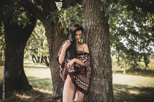 Gypsy girl with long hair posing at nature. A woman with a slim figure and athletic body in knitted sweater, dressed in a sexy kardigan, vintage tones 