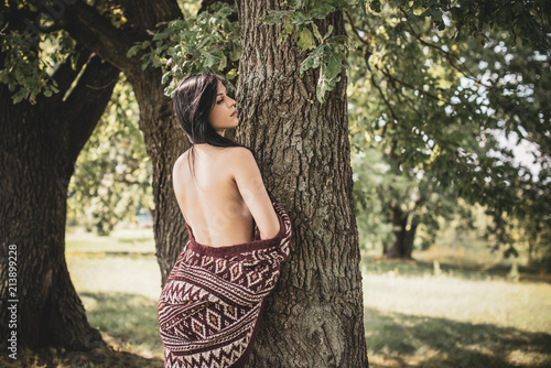 Gypsy girl with long hair posing at nature. A woman with a slim figure and athletic body in knitted sweater, dressed in a sexy kardigan, vintage tones 