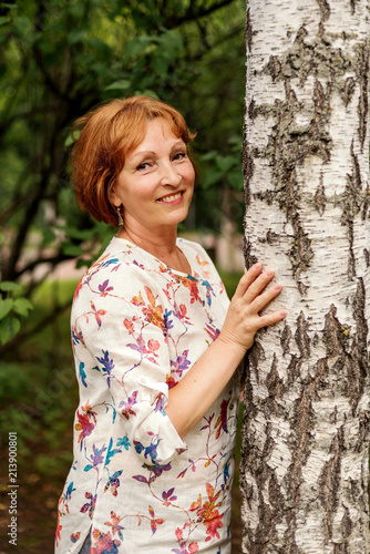 portrait of a middle-aged attractive tranquil woman hugging a birch