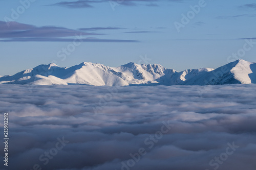 Amazing morning above clouds and fog down in the valley. Snow covered peaks of Tatra mountains peaking through. Feels like flying. Peaceful and relaxing winter vista. Travelling  hiking  adventure.