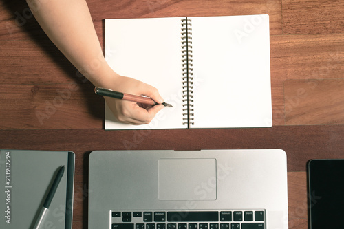 hand holding pen writing on blank page notebook paper. workspce graphic designer top view photo