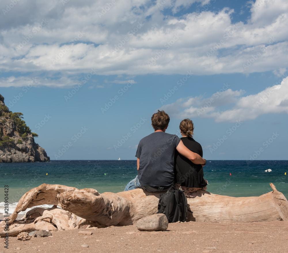 Junges Paar sitzt am Strand auf altem Baumstamm