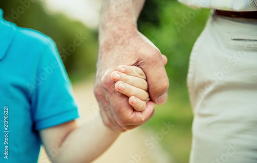 Child holding hand of senior man over a nature background. Two different generations concept.