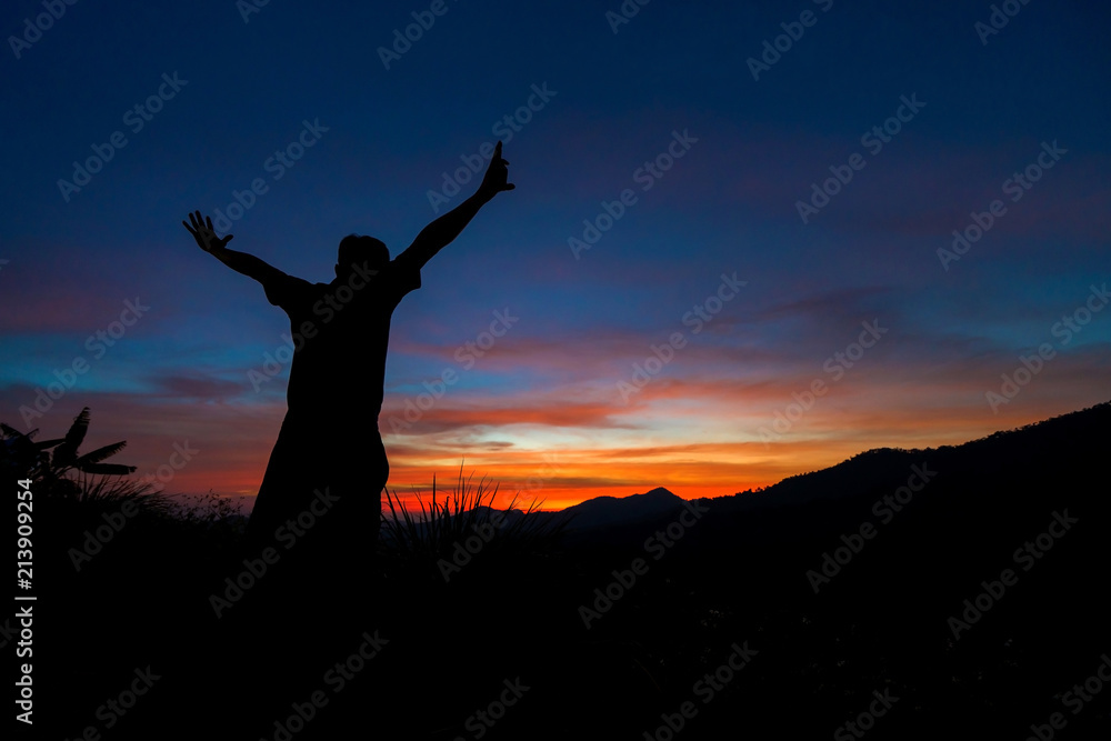 Silhouette of traveler with hands up in the sunset on the mountain