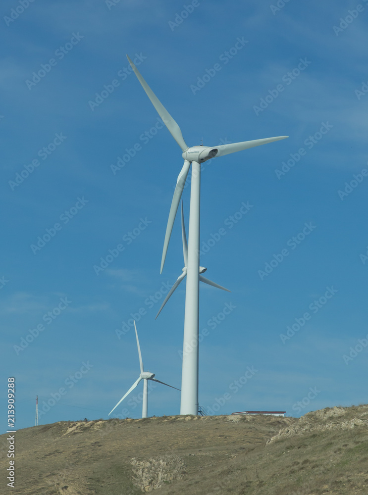 Wind farm: Industrial Eolic installation . Wind turbines towers again cloud blue sky on a wind farm sustainable, renewable energy concept. Alternative energy source from wind power. Wind farm: Industrial Eolic installation . Wind turbines towers again cloud blue sky on a wind farm sustainable, renewable energy concept. Alternative energy source from wind power.