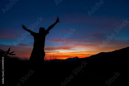 Silhouette of traveler with hands up in the sunset on the mountain