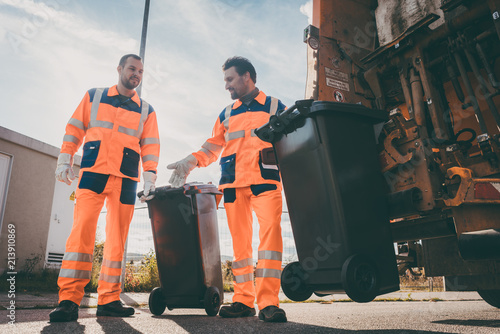 Garbage removal men working for a public utility emptying trash container photo