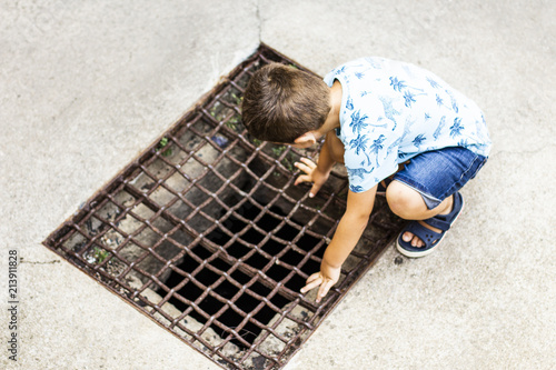 Little boy looking through the grig of a gap on the ground photo