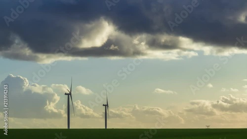 Time lapse of spinning wind turbines for electrical power generation at beautiful sunset with cloudy sky in Normandy, France. Modern technology of environment friendly energy production