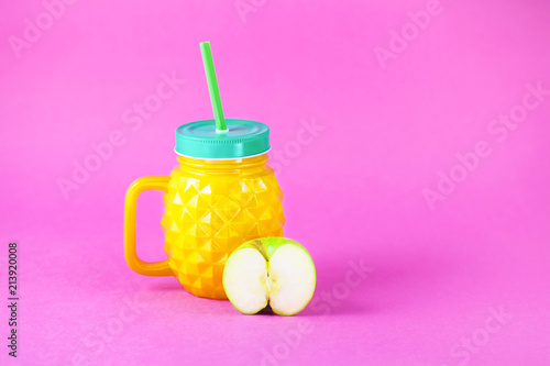 a bottle of pineapple with juice and a piece of apple on a bright rose background Copy space photo