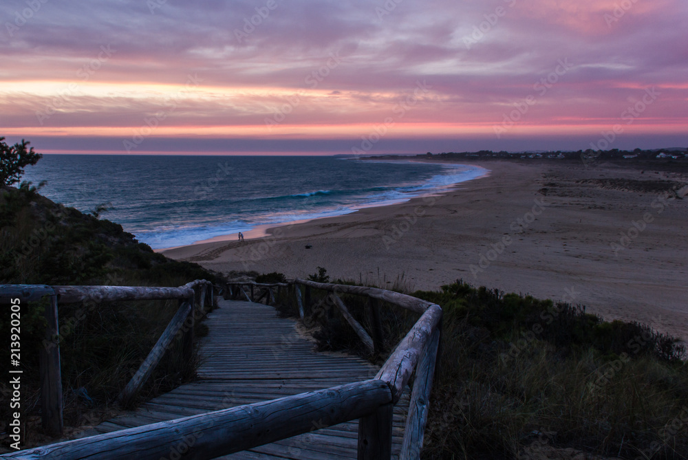 Fototapeta premium Drewniana promenada prowadząca w dół do pustej plaży Zahora o ładnym zachodzie słońca w Kadyksie w Hiszpanii. Wspaniały zmierzch nad morzem w Andaluzji. Letnie wakacje, koncepcje turystyczne