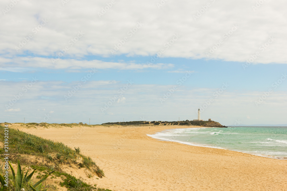 Empty beach of Zahora in low season with Trafalgar lighthouse on the background in the province of Cadiz, South of Spain. Natural wild landscape in Andalusia. Tourism travel destination concept
