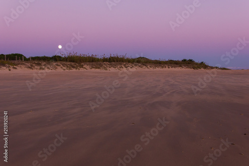 Full moon coming out behind sand dunes at sunset on empty beach in Zahora, Spain. Wild nature landscape in Andalusia