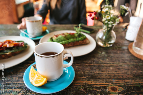 A cup of fresh fragrant tea and next to it nutritious and delicious toast and sandwiches lie on the table. The girl takes a morning breakfast in a cozy cafe