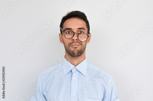 Portrait of frustrated puzzled male with stubble, frowns face, wearing round spectacles posing over white studio background, expresses negative emotion. People, dislike, facial expressions concept