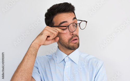 Closeup image of handsome bored sleepy unshaven male after long overwork in office, wants to sleep, wearing round spectacles and blue shirt isolated on white studio background with copy space.