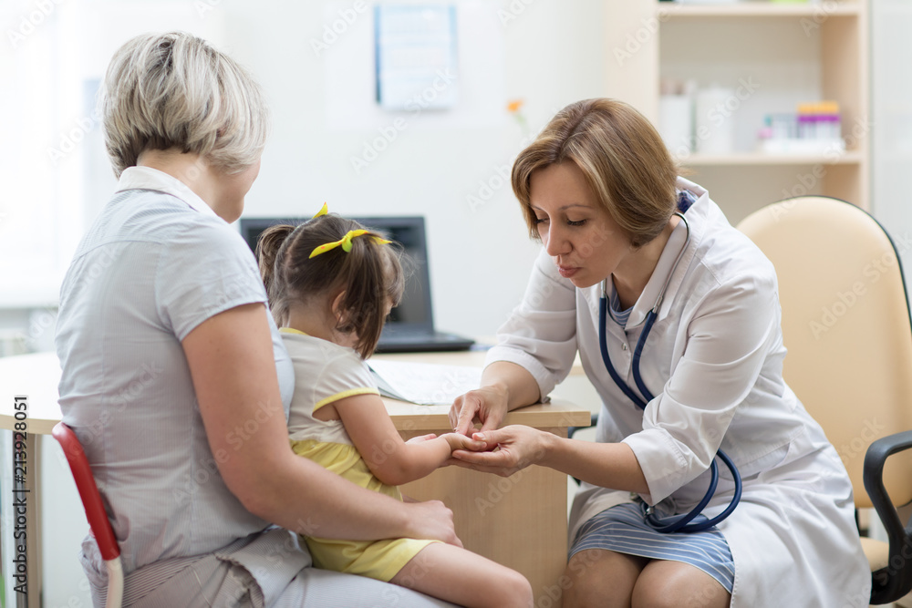 Pediatrician doctor holding kid's hand in her hands. Child girl sitting at mother's knees Pediatrician doctor holding kid's hand in her hands. Child girl sitting at mother's knees