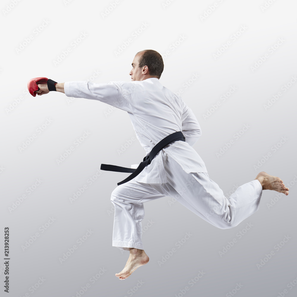 On a light background, an athlete in karategi trains a jab in jump