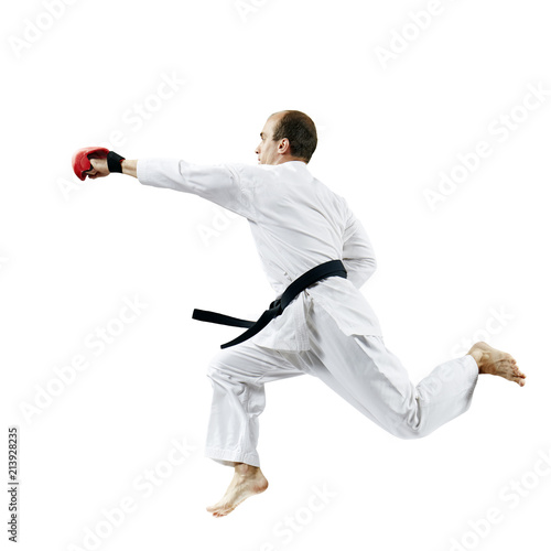 On a white background, an adult athlete in karategi beats with a hand in the jump