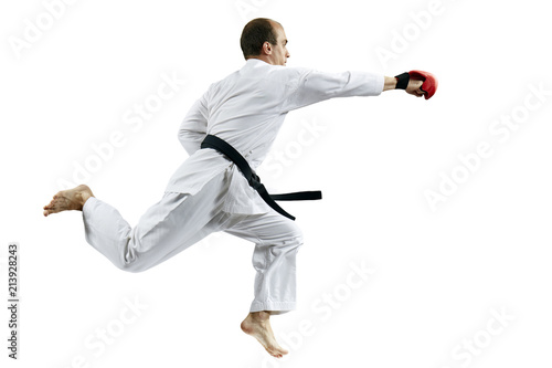 On a white background, an adult athlete in karategi is training blow hand in jump