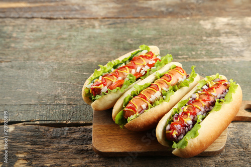 Hot dogs with ketchup, mustard and vegetables on wooden table