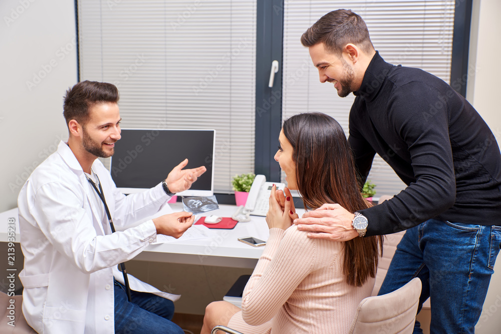 A handsome male doctor shows ultrasound picture to the young pregnant couple. A handsome male doctor shows ultrasound picture to the young pregnant couple.