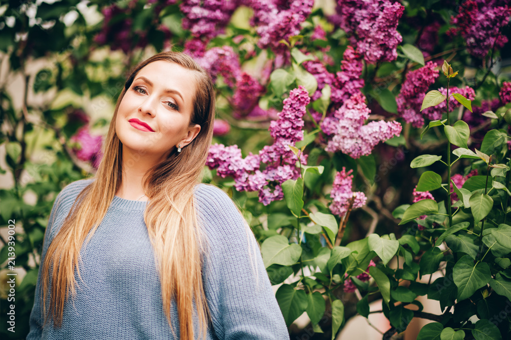 Spring portrait of young beautiful woman wearing blue over size pullover, posing in lilac garden Spring portrait of young beautiful woman wearing blue over size pullover, posing in lilac garden