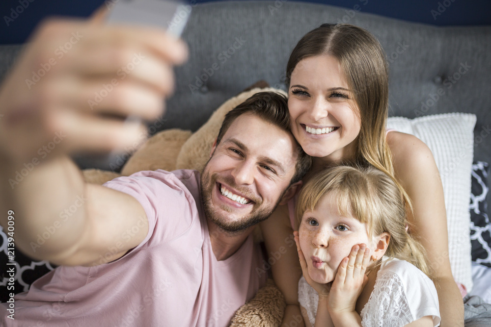 Happy family sitting on bed, taking smartphone selfies Happy family sitting on bed, taking smartphone selfies