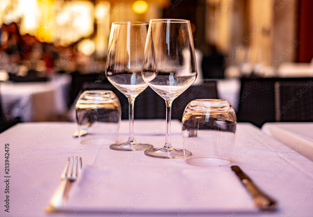 served restaurants table with empty wine glasses, fork and knife on white tablecloth on blur background in sunset