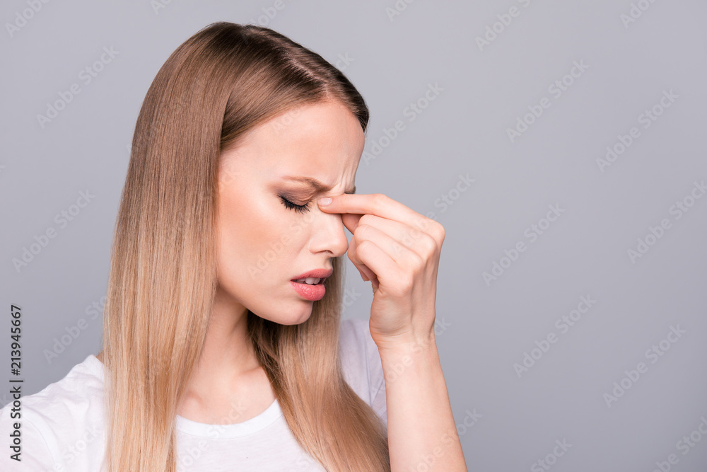 Close up portrait of exhausted young woman, holding her nose bridge with closed eyes, she is tired and depressed isolated on gray background Close up portrait of exhausted young woman, holding her nose bridge with closed eyes, she is tired and depressed isolated on gray background