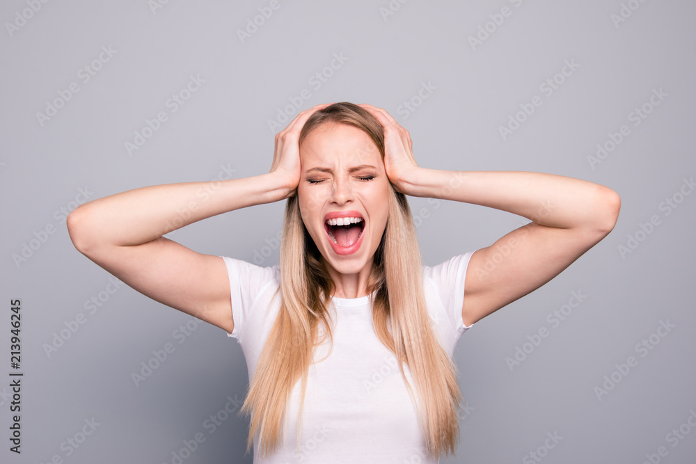 Fototapeta premium Portrait of young blonde attractive gorgeous caucasian charming girl overreacting screaming loudly touching head with hands. Isolated over grey background