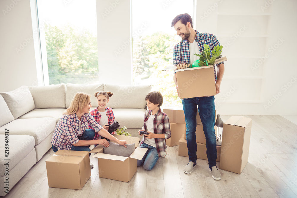 Young happy smiling family unpacking boxes with plants, pillows, stuff, moving to new home, new place of living Young happy smiling family unpacking boxes with plants, pillows, stuff, moving to new home, new place of living