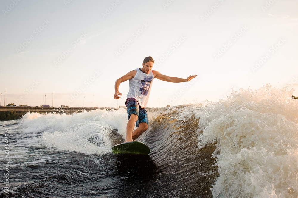 Athletic and young man riding on wakesurf down the river waves