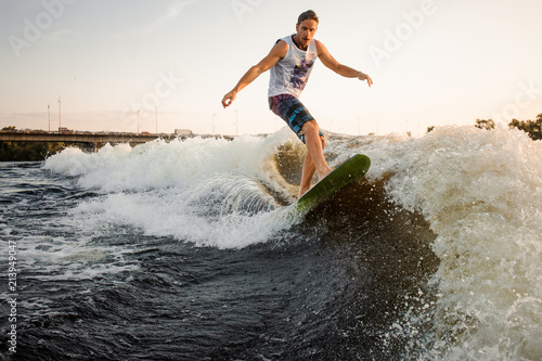 Active and young man riding on wakesurf down the river waves